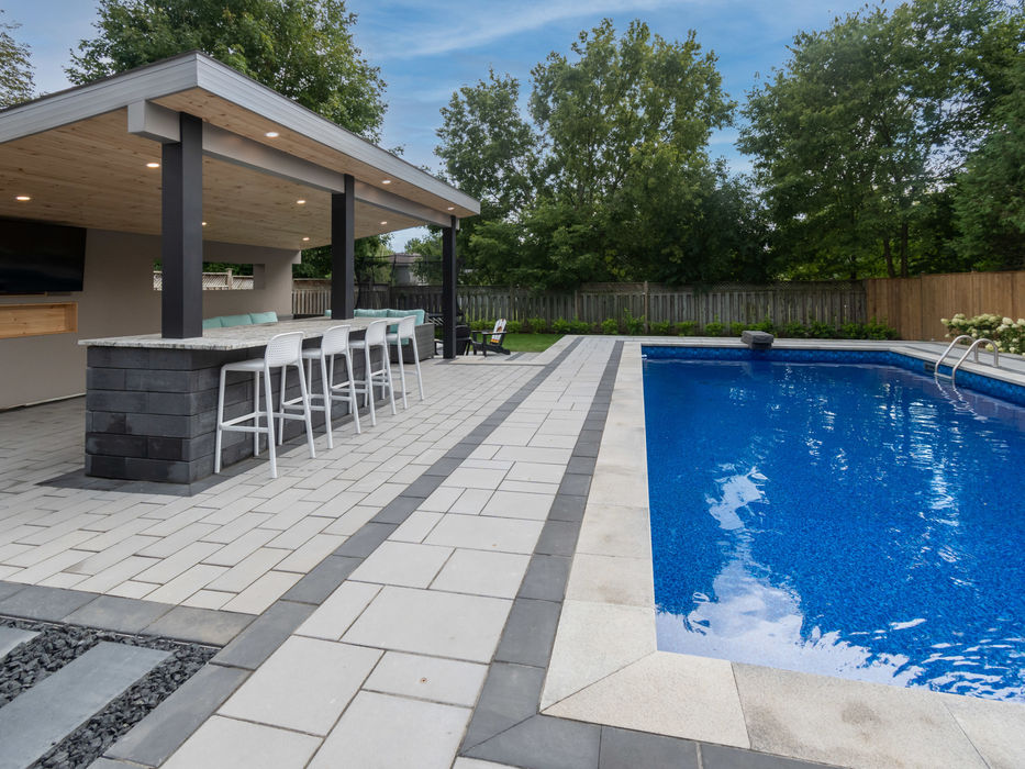 Luxury timber-framed gazebo with a built-in stone bar and outdoor kitchen overlooking a bright blue geometric pool.