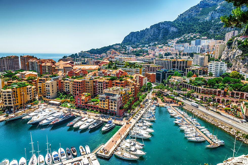 Vue panoramique du port de Monaco avec des yachts, des bâtiments et un arrière-plan montagneux.
