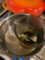 The oil and cottonwood salve in a glass jar that is placed in a pot of boiling water to create a water bath