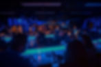 Dimly lit nightclub with a crowd seated at glowing blue tables, engaged in conversation. Blue lighting adds a lively atmosphere.