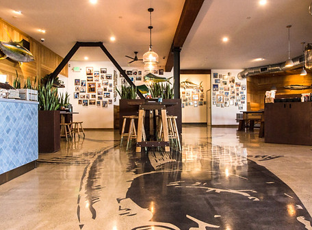 blue water seafood interior, sand color tile floor with giant fish graphic on floor, photos of local friends on back wall,