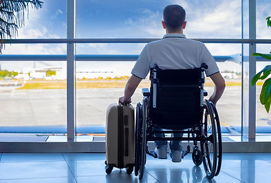 Person in wheelchair looking out an airport window with a suitcase in hand