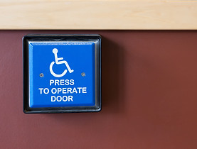 Automated door opening button with handicap sign reading "Press to operate door"