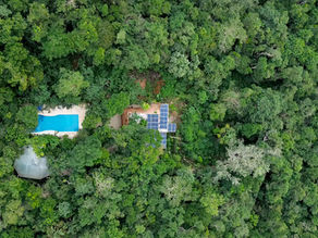 Aerial view showcasing Lunita, nestled within dense green forest, featuring a solar panel installation and a pool peeking through the lush canopy, making it an ideal location for a digital detox retreat.
