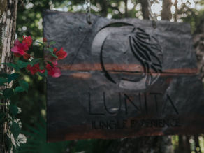 Entrance to the Lunita Jungle Corporate Retreat Center in Mexico, featuring a rustic sign surrounded by lush greenery and vibrant red flowers.