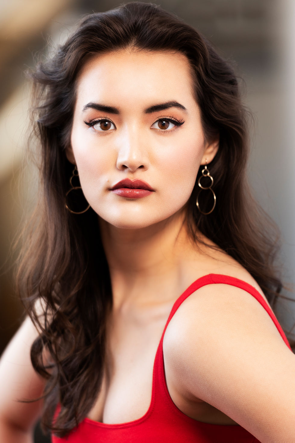 Portrait of a woman with dark hair, red top, and hoop earrings