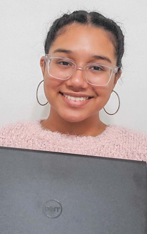 Smiling young woman wearing clear glasses holds a black Dell laptop.