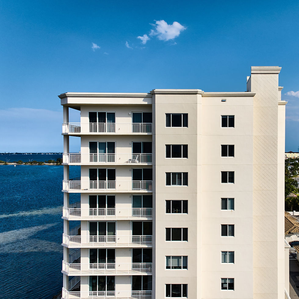 Tall white building with balconies beside a body of water under a blue sky.