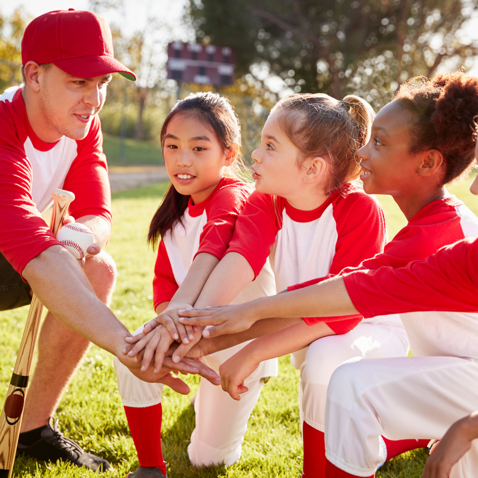 Youth baseball team and coach huddle with hands together.