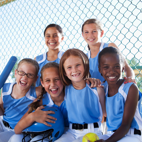 Team of smiling young girls in softball uniforms with equipment