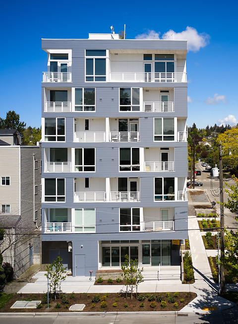 Modern high-rise building with many windows and balconies. Street view, sunny day.
