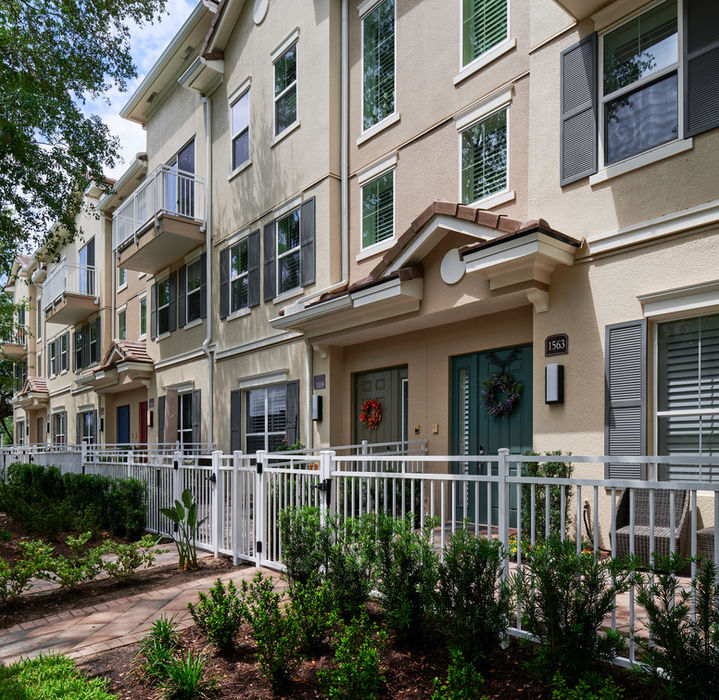 Row of townhomes with windows and doors; white fence in front.