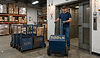 Worker moving a 500lb blue cart into a warehouse elevator