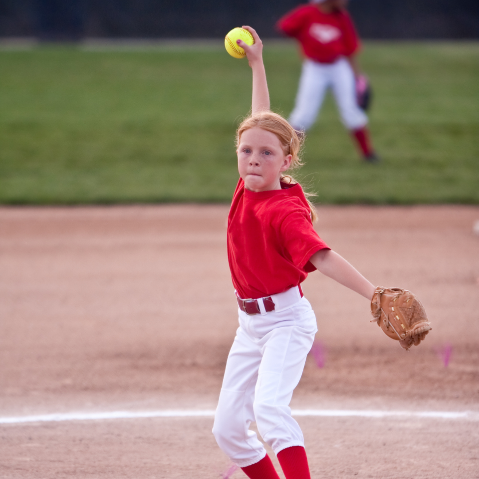 Girl in red uniform pitching a softball