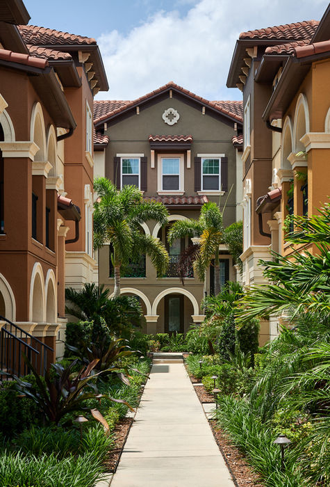 Pathway through colorful buildings, lush greenery, and archways under a bright sky.
