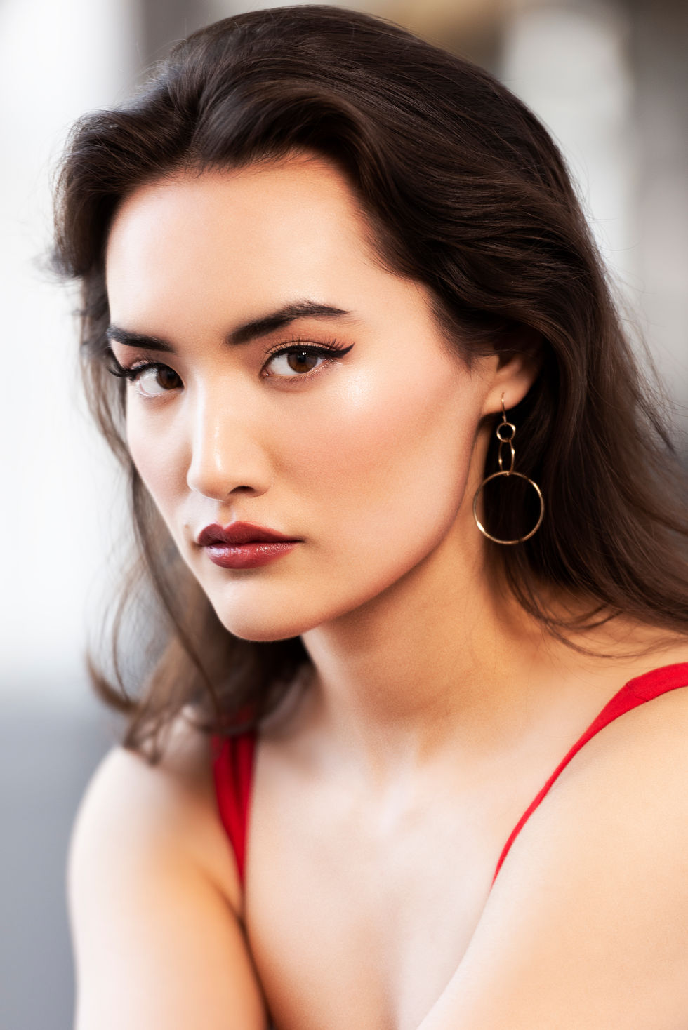 Woman with dark hair, red top, and circular earrings