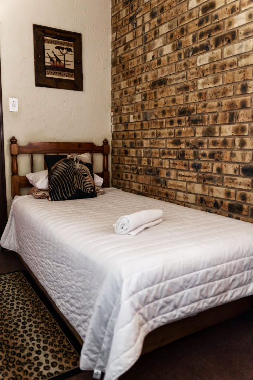 Single guest room with white bedding, zebra cushion, and rustic brick feature wall