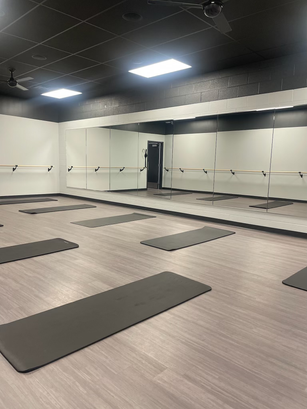 Bright and serene yoga studio at Rhythm Cycle & Sculpt, featuring clean floors, soft lighting, and rental yoga mats neatly arranged for class.