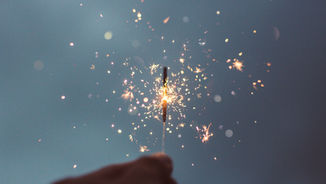 Sparking fireworks against a dark blue sky create a vibrant explosion of light and color, with glowing particles scattered throughout.