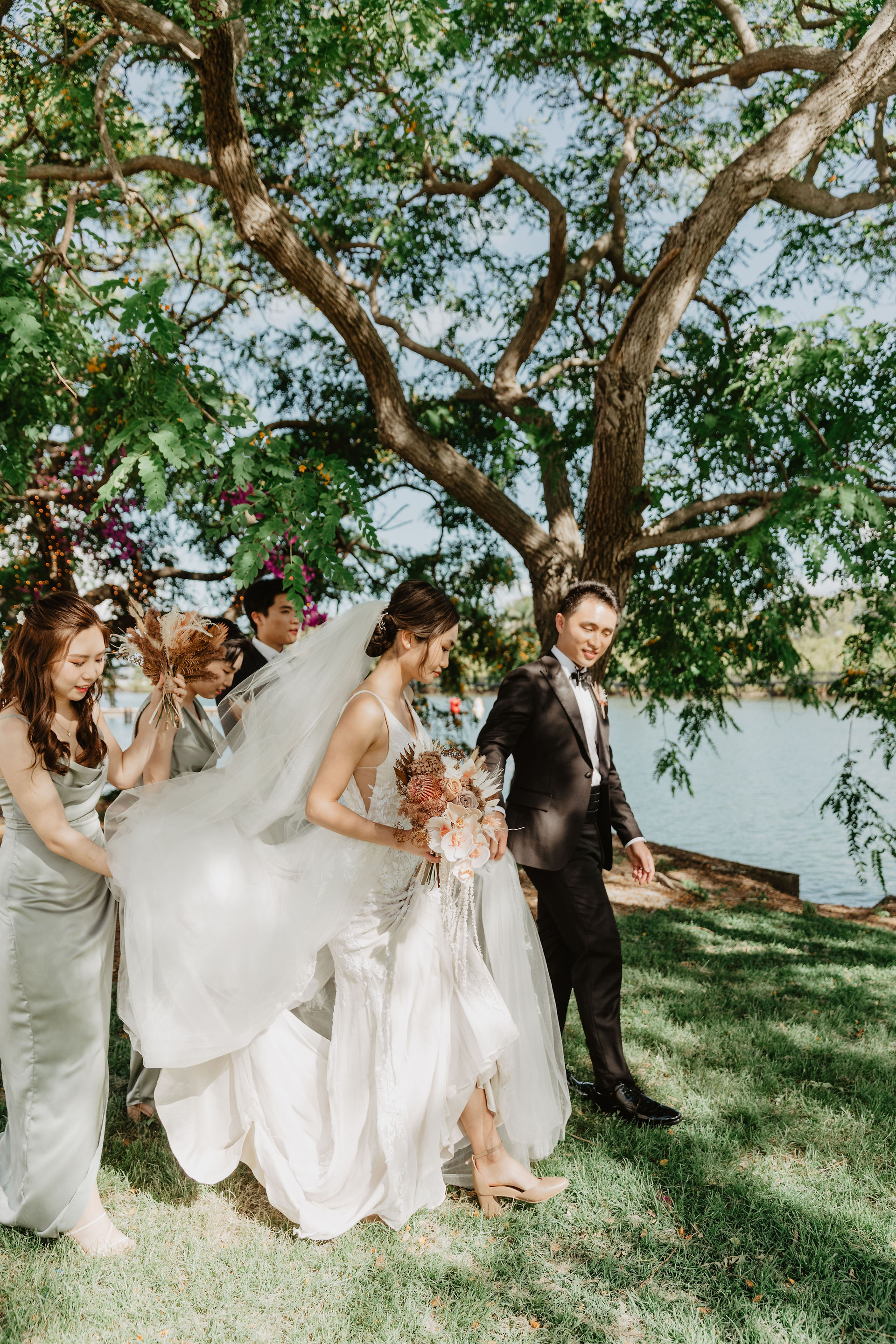 candid shot of bride and groom walking with bridal party to photo spot by a lake