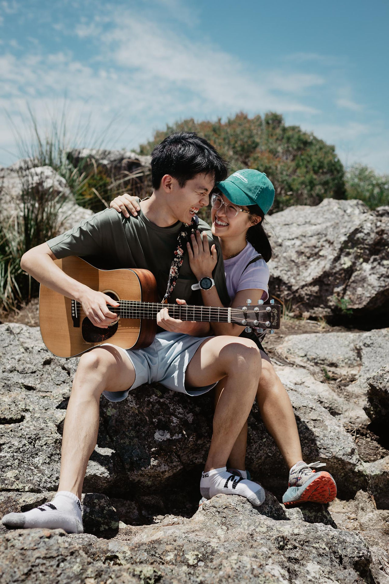 Asian guy playing acoustic guitar for girlfriend on mountain