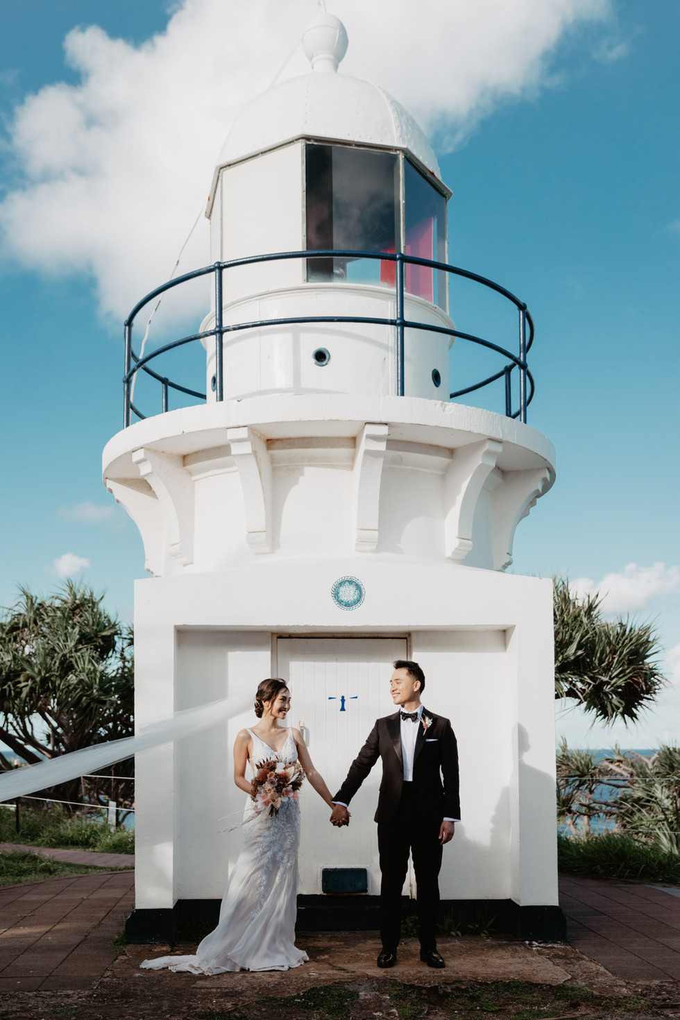 asian bride and groom holding hands at fingal head lighthouse