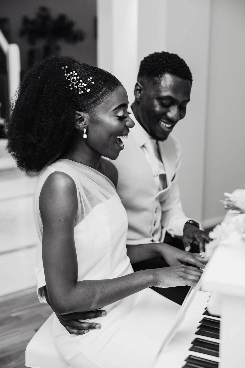 african wedding couple playing white grand piano together laughing