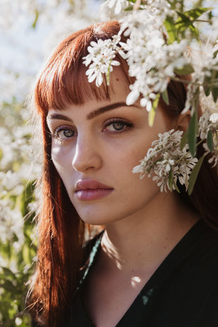 creative outdoor headshot of red head female actress with white flowers