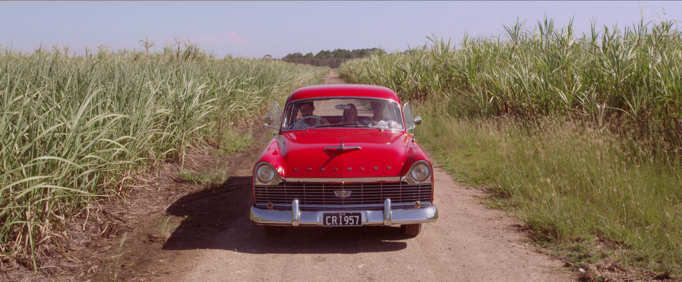 red 1950s christler in cane field jacob's well dusty road