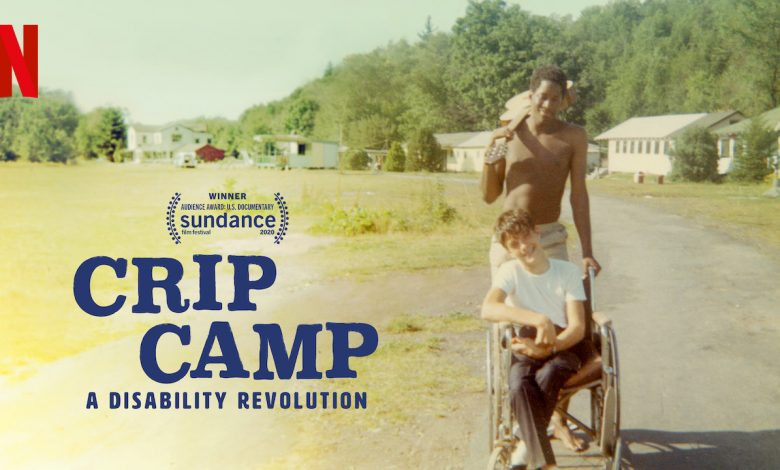 Crip Camp. A Disability Revolution. Shows a phto from the 70s. A young man with no shirt and a guitar over his shoulder pushes a teenage boy in a wheelchair. They are both smiling with a background of cabins, grass and trees. In the corner is the Netflix logo, and a logo indicating it was the Winner of the Audience award at the Sundance Film festival.
