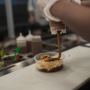 Almond butter being drizzled on an acai bowl in the line by an employee