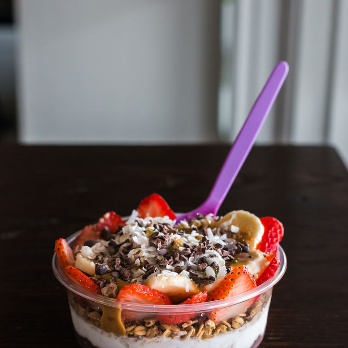 Acai bowl with acai and coconut base, topped with granola, peanut butter, strawberries, banana, cacao nibs, and coconut flakes.