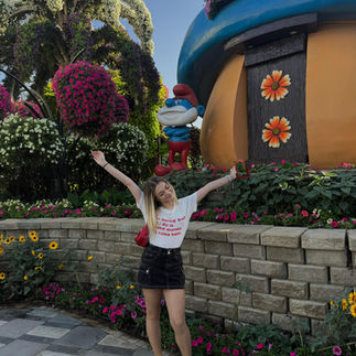Dubai Miracle Garden’da Şirinler temalı çiçek süslemeleri önünde poz veren ziyaretçi.
