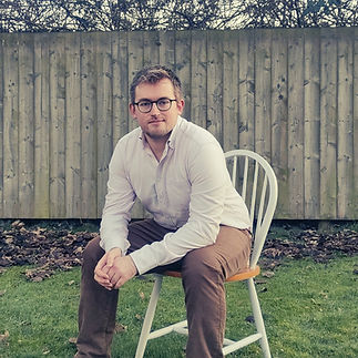 An image of Cameron, sat outside, and leaning forwards in his chair.