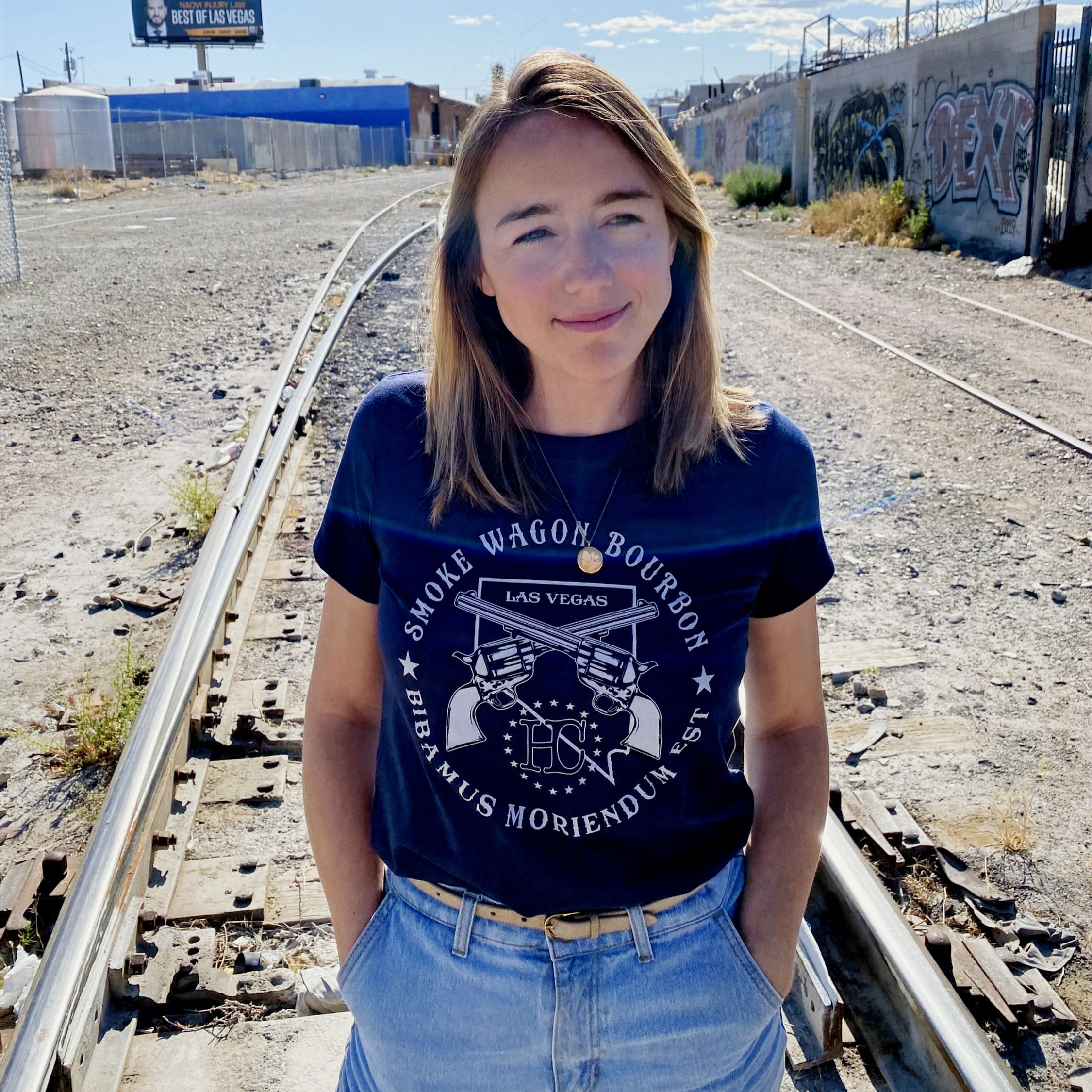 Smoke wagon logo in silver on a navy tee worn by Lynsey gazing off