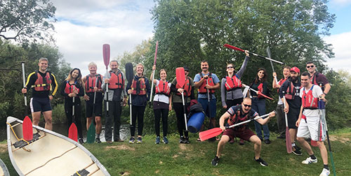BIOS Team lined up next to a canoe. All happily holding oars and wearing life jackets.