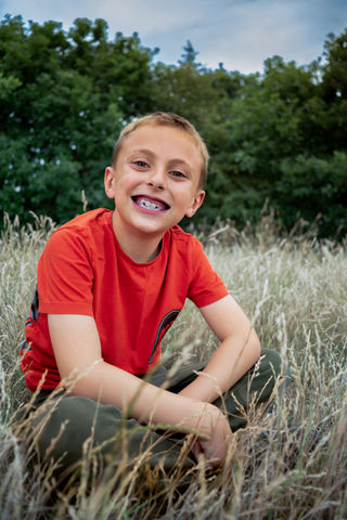Smiling child in red shirt sitting in grass.