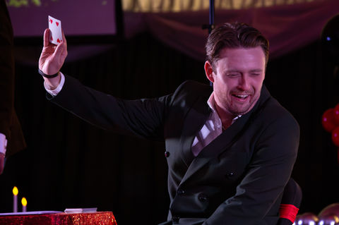 Man holding a playing card, smiling during performance.