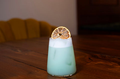 Green cocktail with a candied lemon garnish on a wooden table