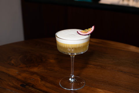 Yellow cocktail with white foam and passion fruit garnish