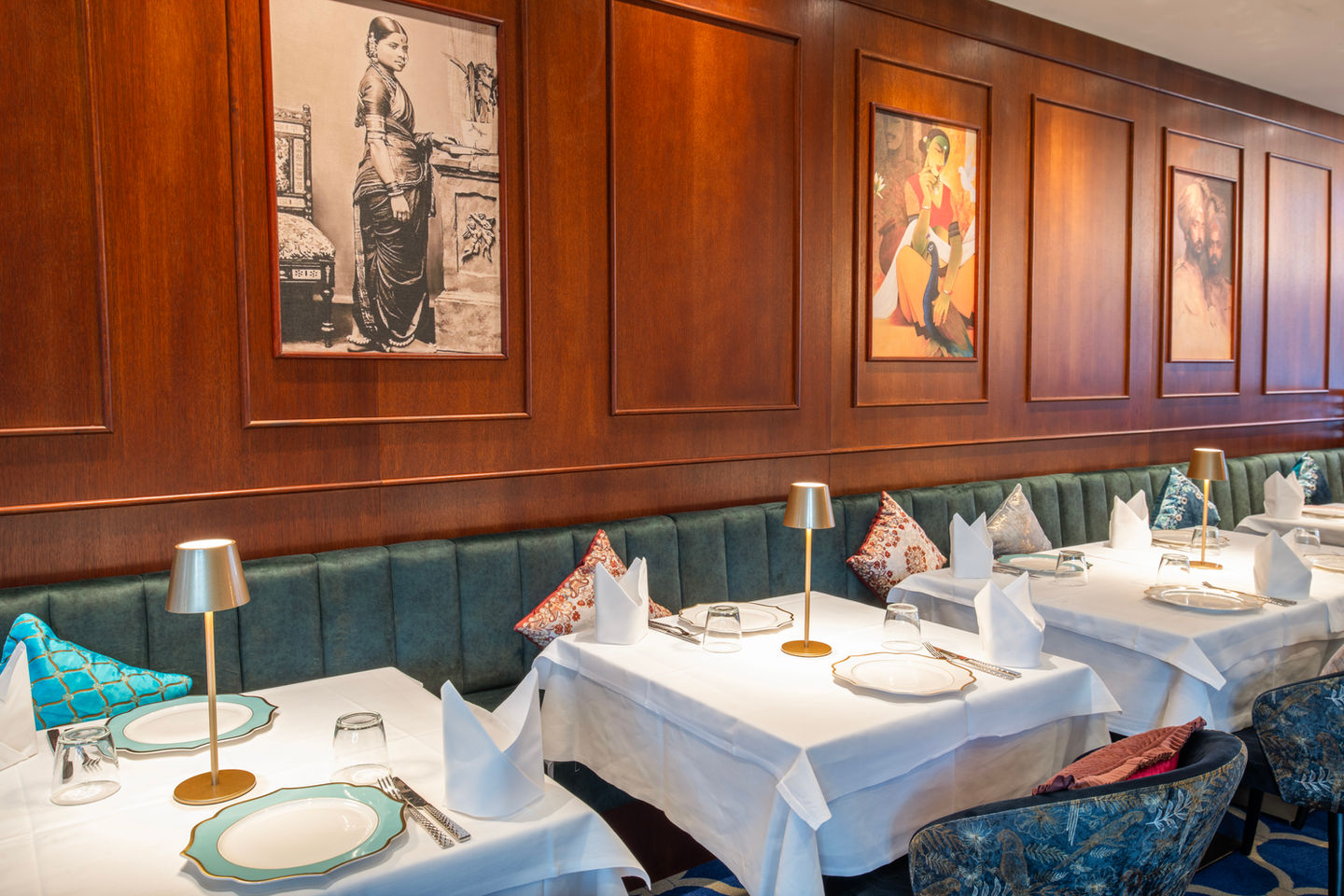 Restaurant dining tables set with white linens, gold lamps, and teal chairs