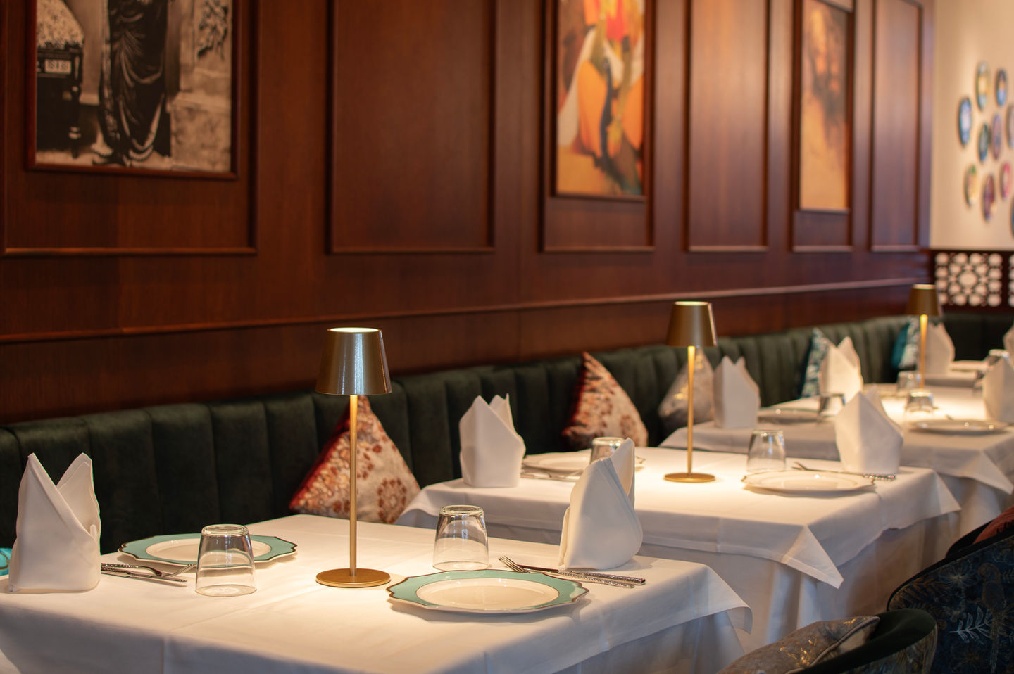 Table setting with plates, glasses, and cutlery in a restaurant with a dark wood wall and green booths