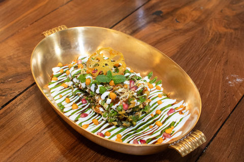 Layered Indian street food dish with yogurt, green chutney, and pomegranate seeds