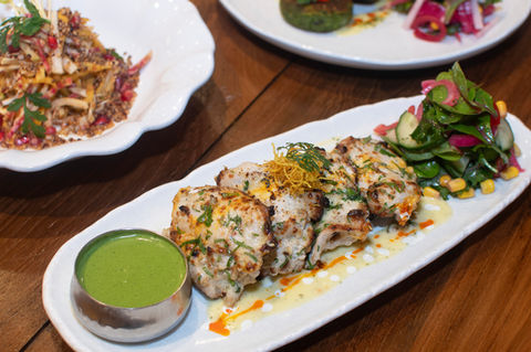 Grilled chicken skewers with green chutney, salad, and sauce on a white plate