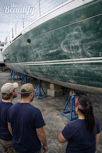 Photo-realistic image of three crew members standing in a boatyard observing a large deep-green sailboat hull elevated on blue jack stands. The hull surface appears heavily oxidized and chalky, with visible sanding marks, scuffs, and uneven coloration indicating severe surface degradation. White accent stripes run along the hull, contrasting with the faded green finish. The surrounding gravel yard and nearby vessels reinforce the working marina environment. The We Beautify Boats by Spike logo is positioned in the upper left corner. The image represents a pre-restoration condition requiring Level 5 hull polishing with full wetsanding and multi-stage correction to restore a mirror-like finish. Service by We Beautify Boats by Spike, Boat Detailing, Toronto, Ontario, Canada.