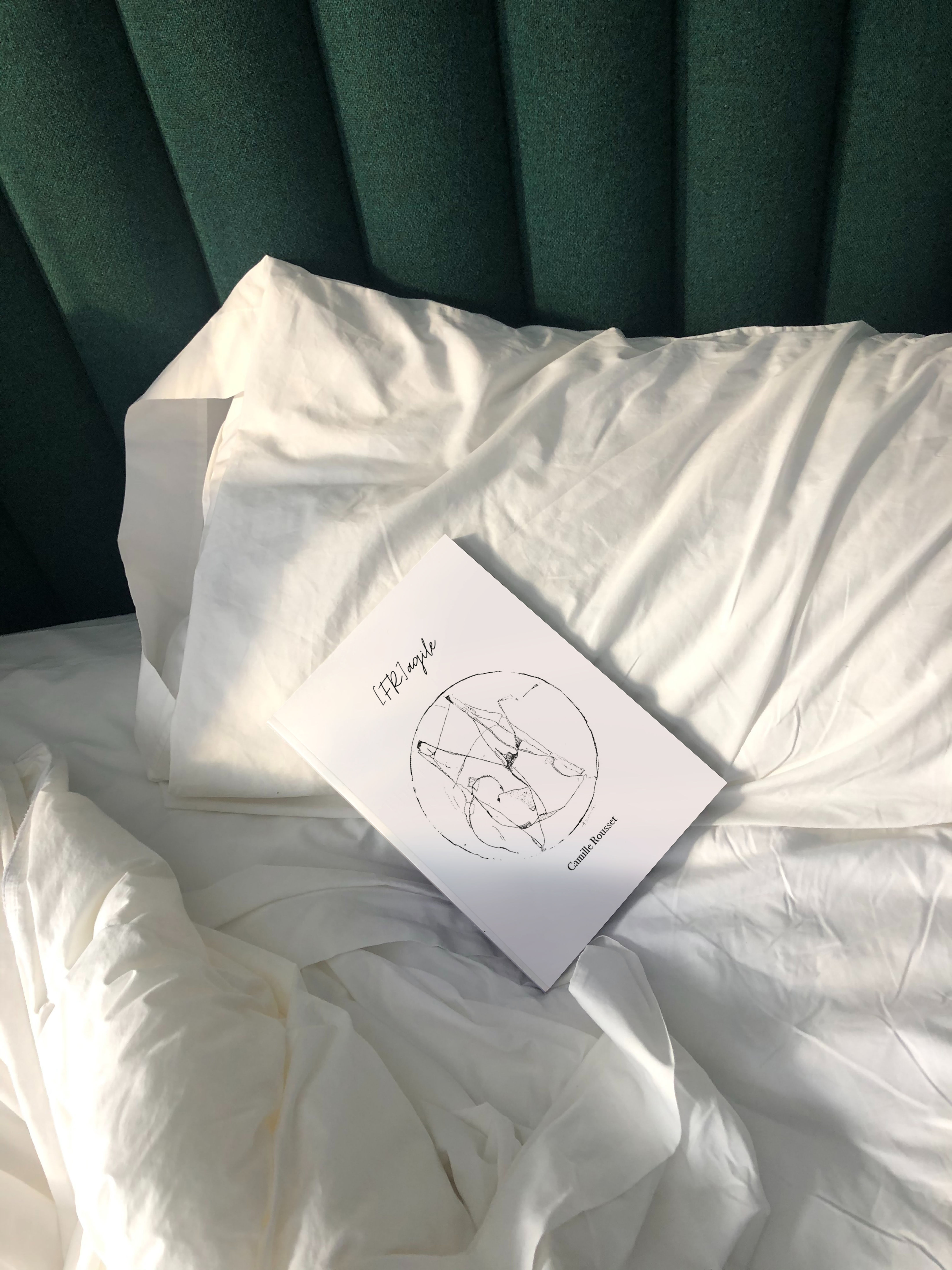Livre Fragile par Camille Rousset posé sur un lit défait.