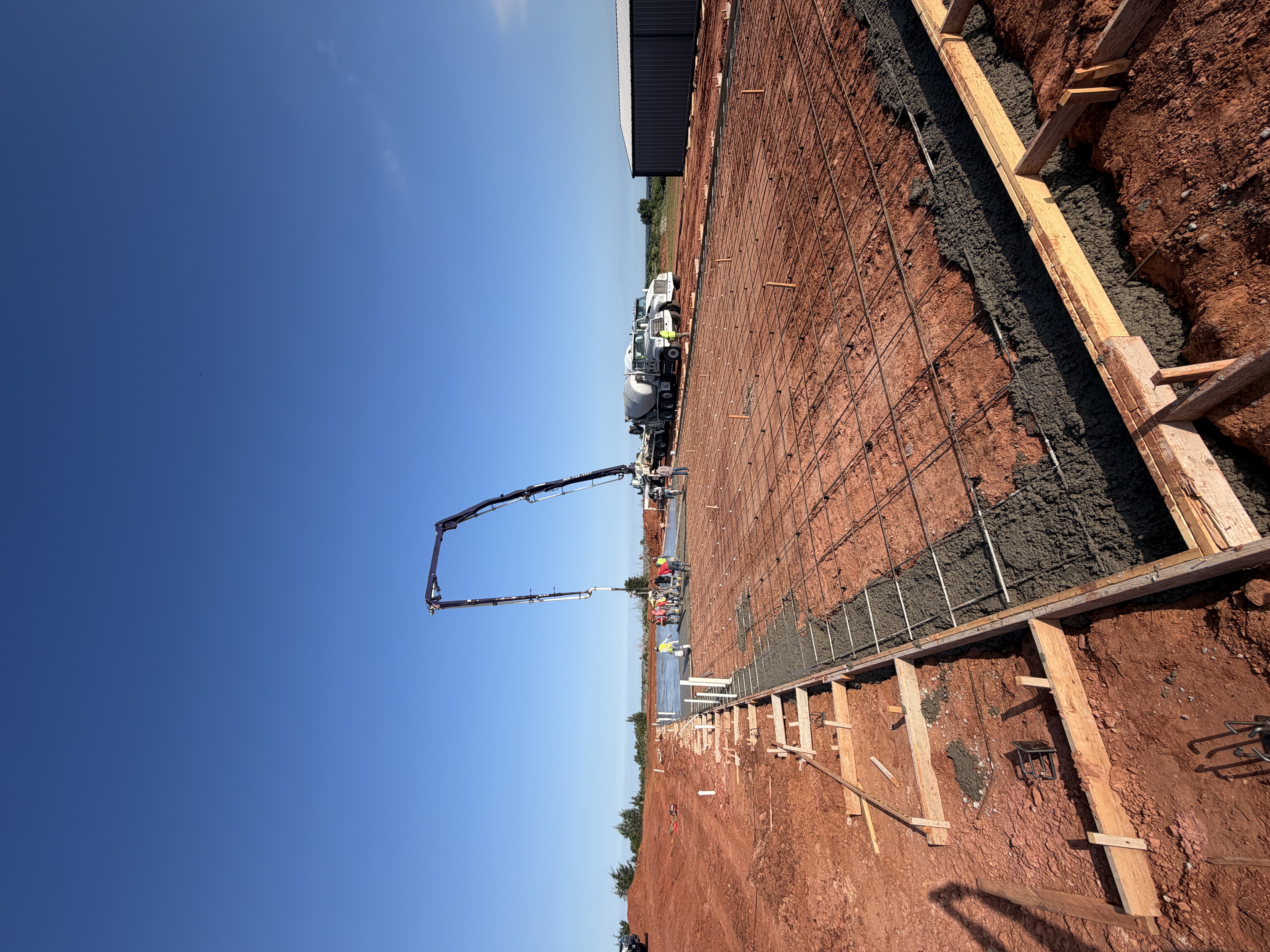 Concrete pump pouring a slab with rebar and forms beside a metal building