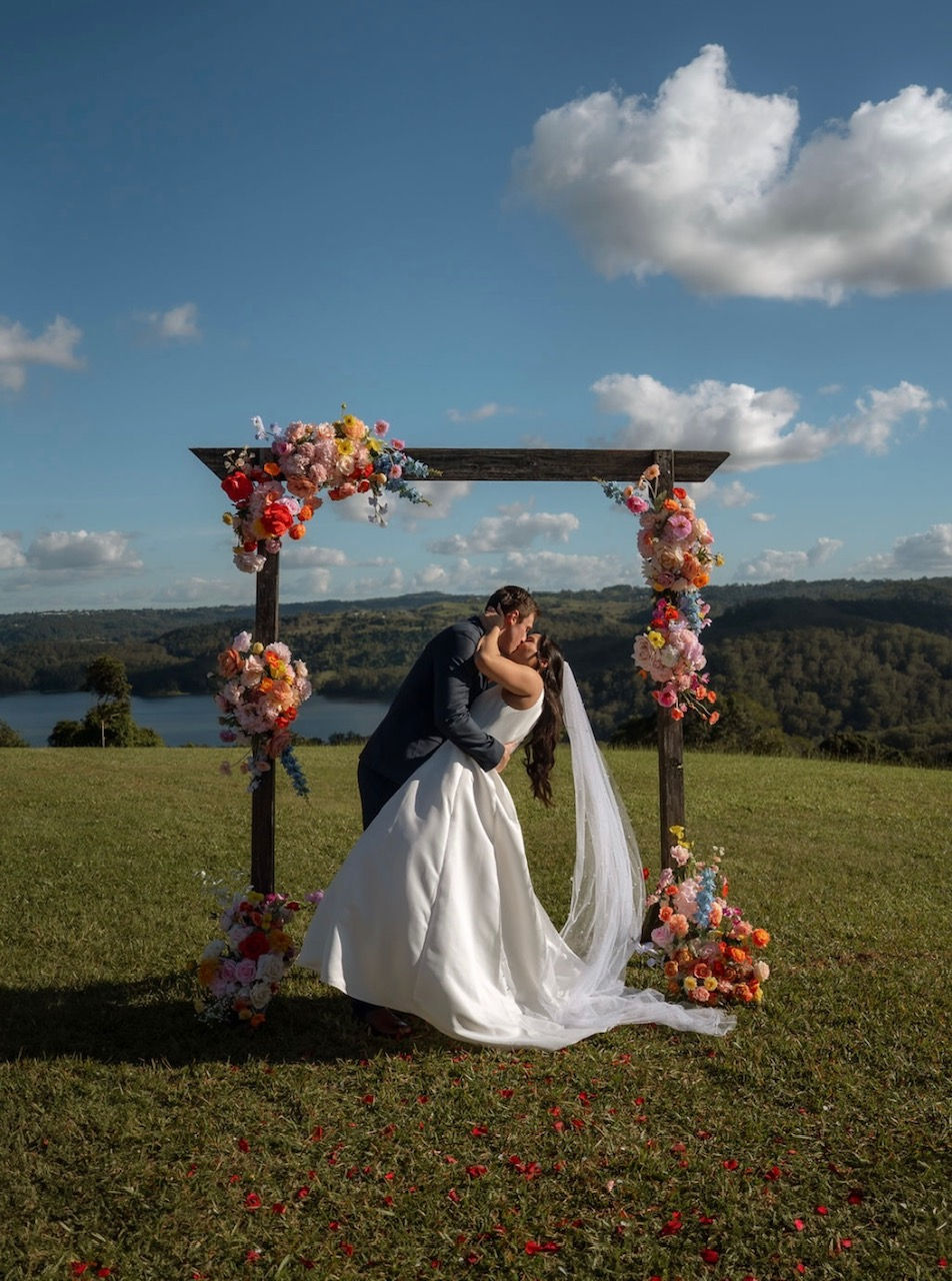 Couple embrace under the wedding arbour on a stunning day at the Lakehouse Folk Montivlle Queensland