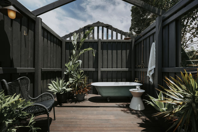 Antique bath outdoors with privacy in a garden setting with black fencing and plants