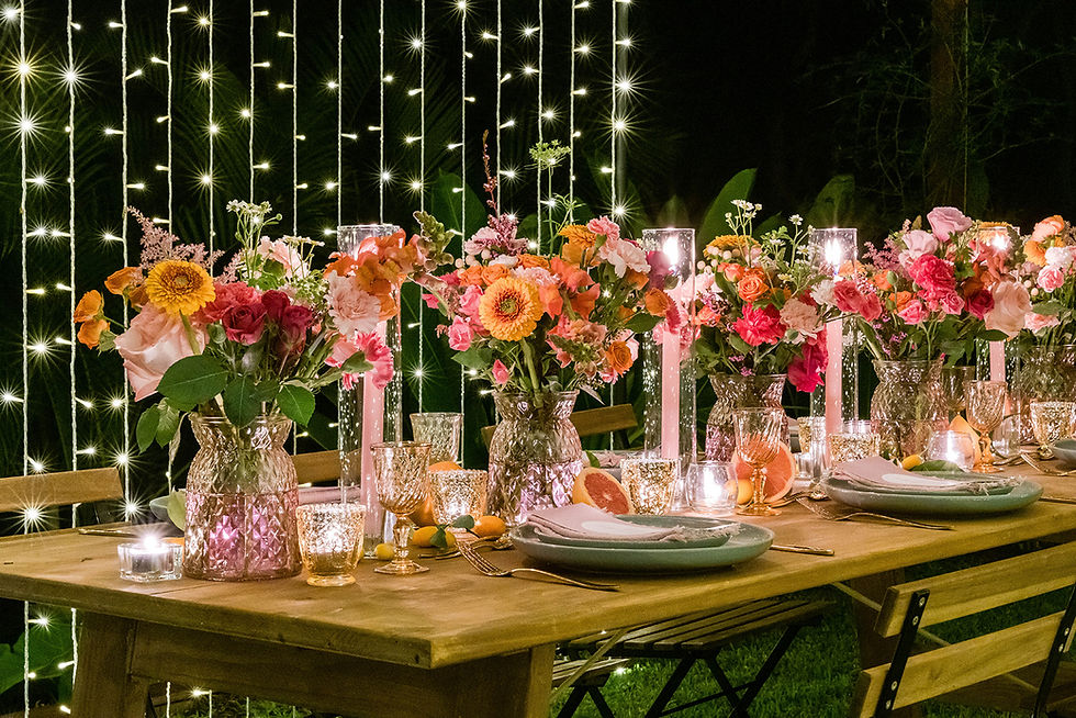 Elegant outdoor table set with colorful flowers, lit candles, and hanging string lights, creating a warm, festive ambiance for weddings.
